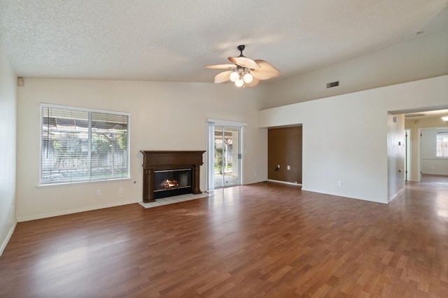 unfurnished living room featuring a wealth of natural light, visible vents, a fireplace with flush hearth, a ceiling fan, and wood finished floors