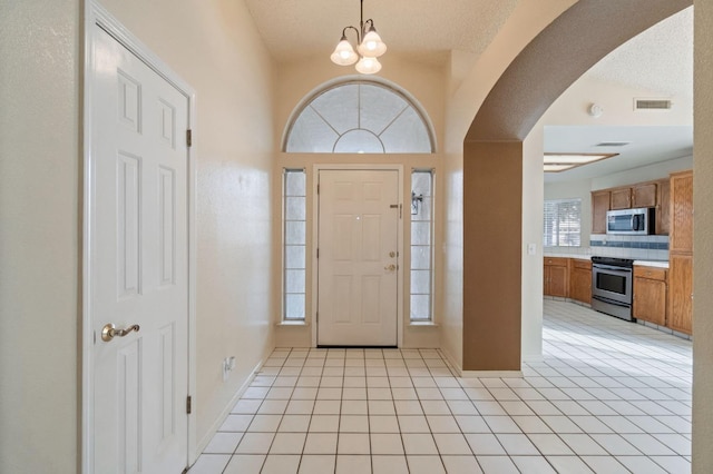 entrance foyer with arched walkways, light tile patterned floors, a chandelier, and visible vents