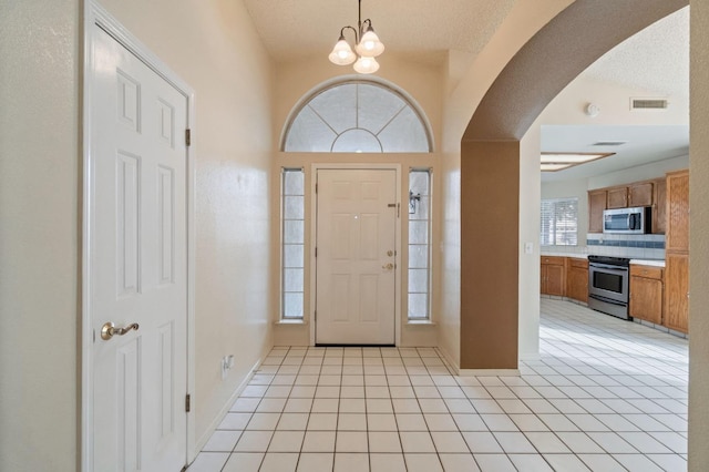 entrance foyer with a chandelier, visible vents, arched walkways, and light tile patterned floors