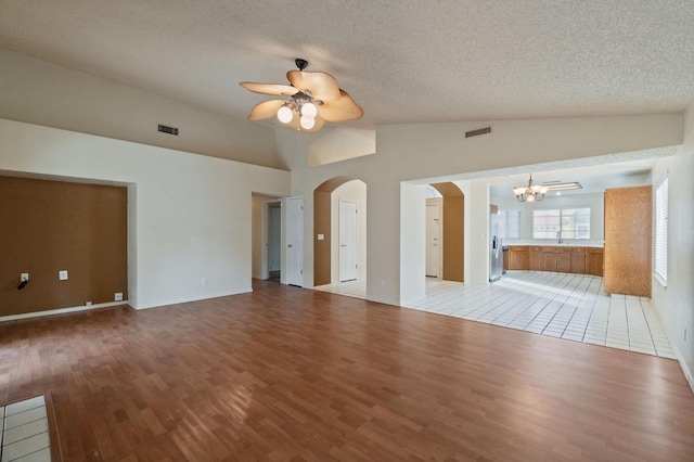 unfurnished living room with visible vents, arched walkways, ceiling fan with notable chandelier, and lofted ceiling