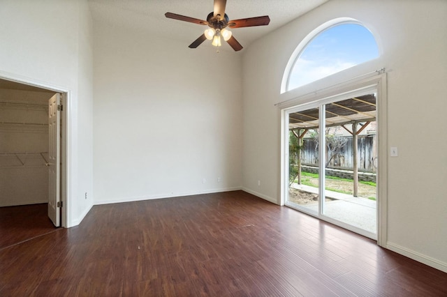 empty room featuring a towering ceiling, baseboards, dark wood finished floors, and a ceiling fan