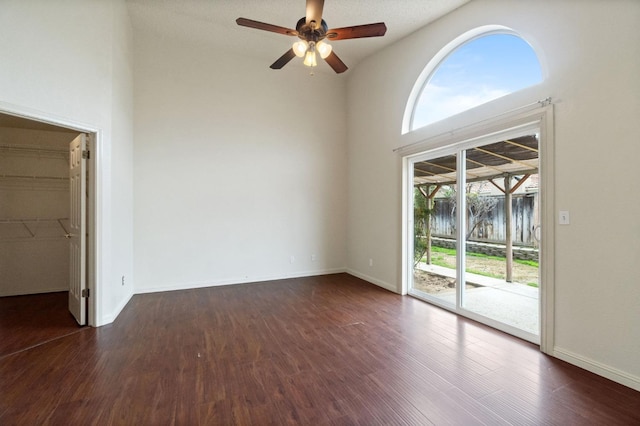 spare room with a high ceiling, ceiling fan, baseboards, and dark wood-type flooring
