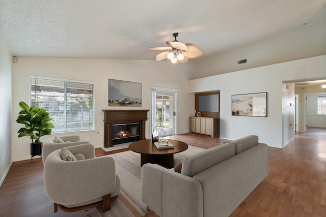 living room with lofted ceiling, a fireplace with flush hearth, visible vents, ceiling fan, and wood finished floors