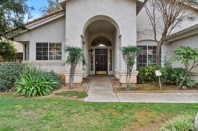 view of exterior entry featuring a yard, a tiled roof, and stucco siding