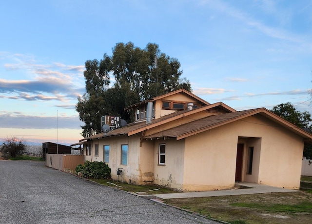 view of front of house with a shingled roof, central air condition unit, and stucco siding