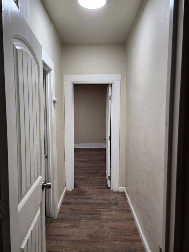 corridor featuring baseboards and dark wood-style flooring