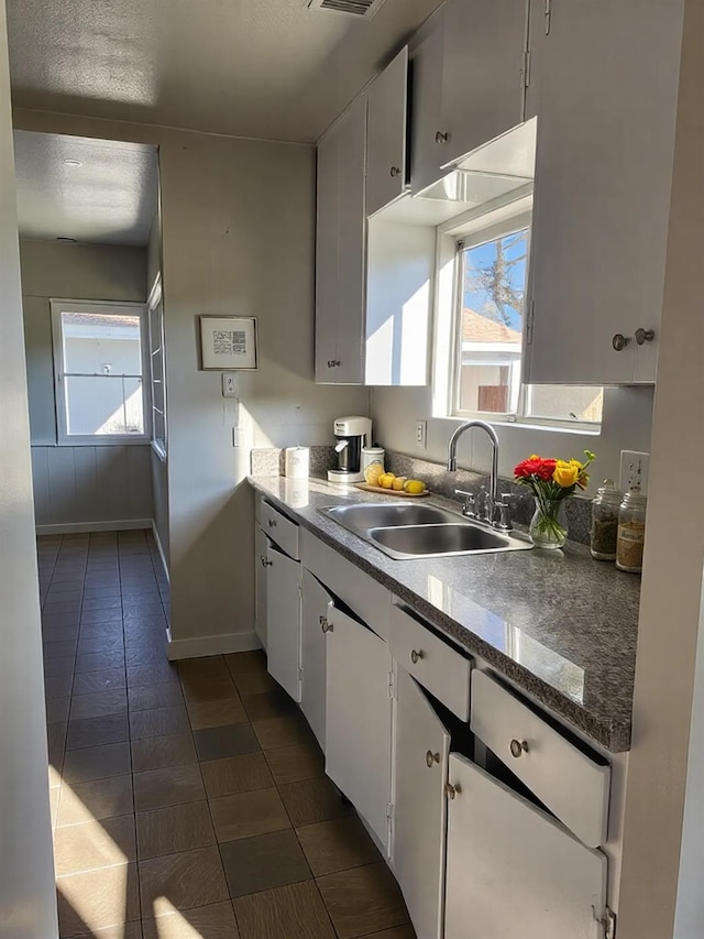 kitchen with baseboards, visible vents, white cabinets, dark countertops, and a sink