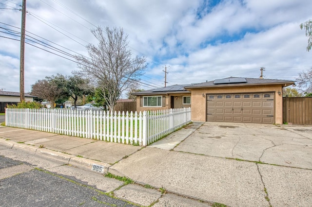 ranch-style home featuring a fenced front yard, an attached garage, driveway, roof mounted solar panels, and stucco siding