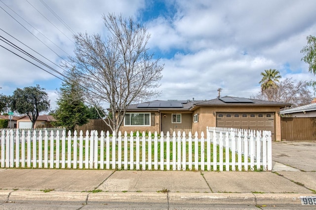 view of front of property featuring an attached garage, a fenced front yard, roof mounted solar panels, and concrete driveway