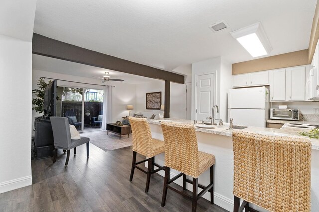 kitchen with a breakfast bar area, dark wood-type flooring, freestanding refrigerator, white cabinets, and a sink