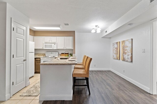 kitchen featuring white appliances, white cabinets, a kitchen breakfast bar, light stone countertops, and a sink