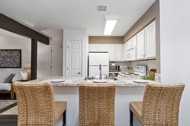 kitchen with white appliances, white cabinetry, a peninsula, and light stone countertops