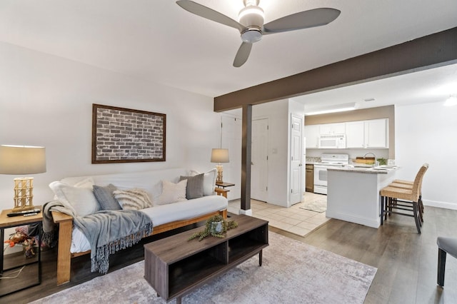 living area with a ceiling fan, light wood-style flooring, and baseboards