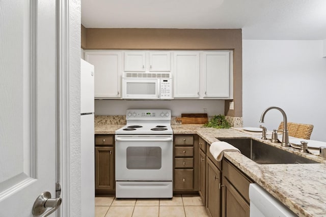 kitchen with light tile patterned flooring, a sink, white cabinetry, light stone countertops, and white appliances