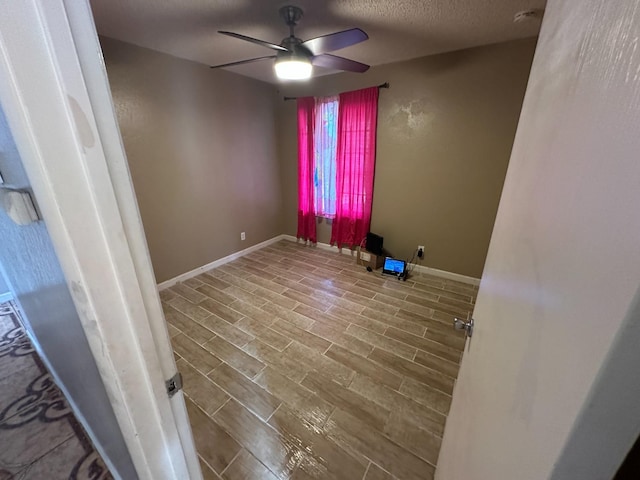 unfurnished room with a ceiling fan, wood finish floors, a textured ceiling, and baseboards