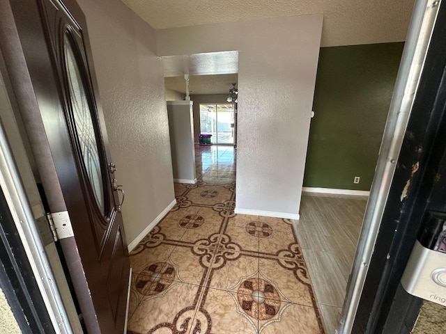 hallway with tile patterned flooring, a textured wall, a textured ceiling, and baseboards