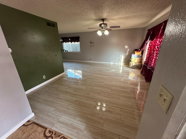 unfurnished room with ceiling fan, a textured ceiling, visible vents, and baseboards