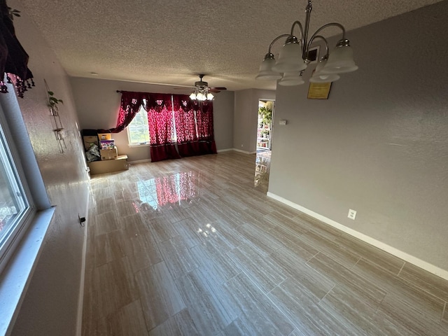 spare room featuring wood finished floors, a textured ceiling, baseboards, and ceiling fan with notable chandelier