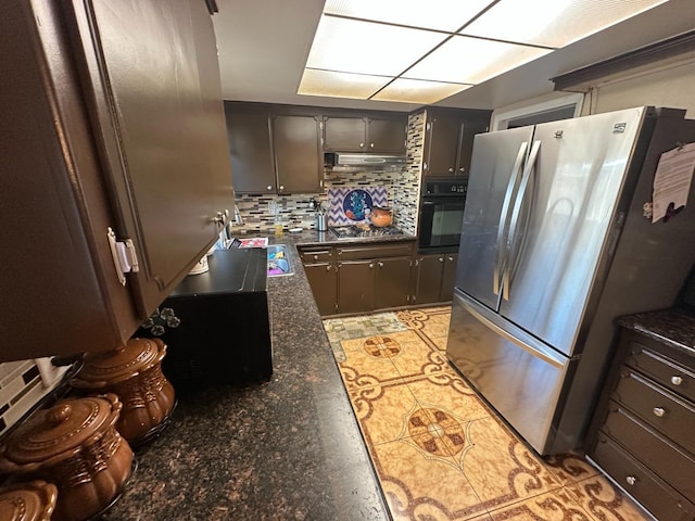 kitchen featuring range hood, stainless steel appliances, backsplash, dark brown cabinets, and dark stone counters