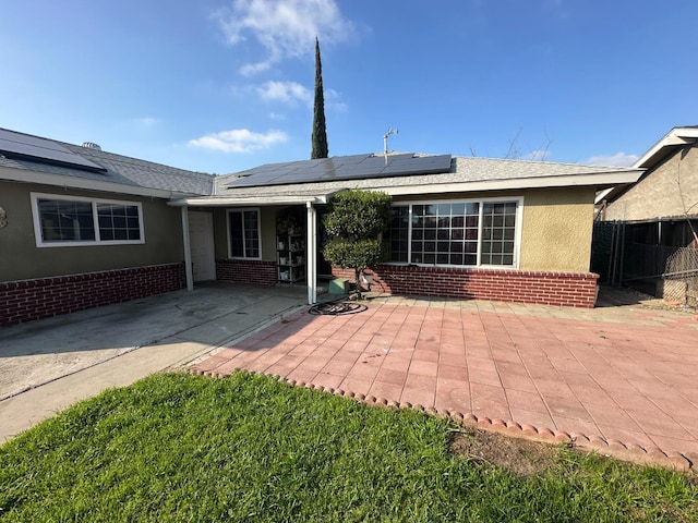 rear view of house with brick siding, stucco siding, solar panels, a patio area, and fence