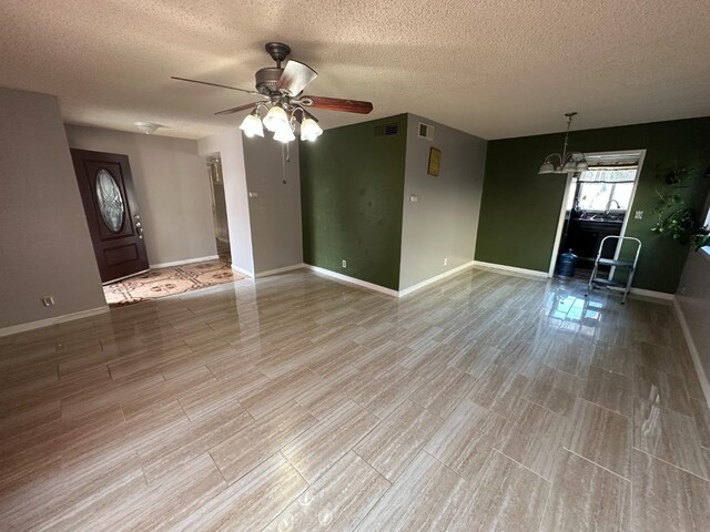 unfurnished living room with visible vents, a textured ceiling, baseboards, and ceiling fan with notable chandelier