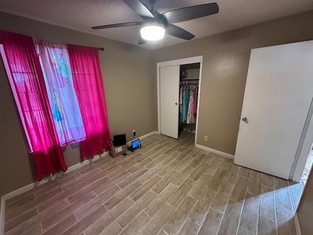 unfurnished bedroom with wood finish floors, a closet, a ceiling fan, and baseboards