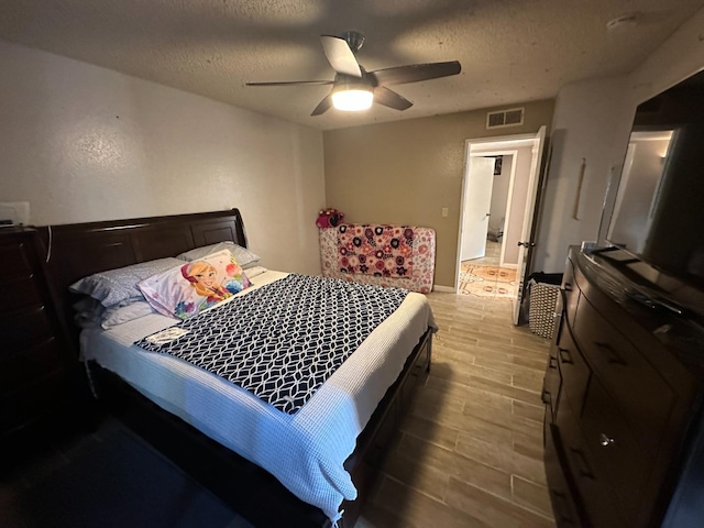 bedroom featuring ceiling fan, visible vents, a textured ceiling, and wood finish floors