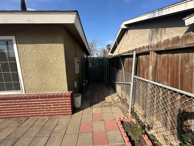 view of side of home featuring brick siding, fence, a patio, and stucco siding