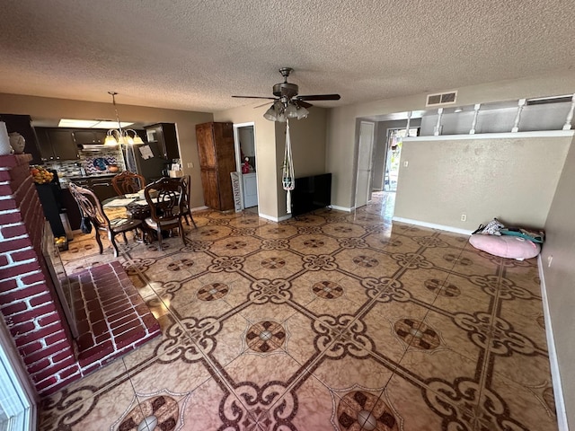 living area featuring visible vents, a textured ceiling, baseboards, and ceiling fan with notable chandelier