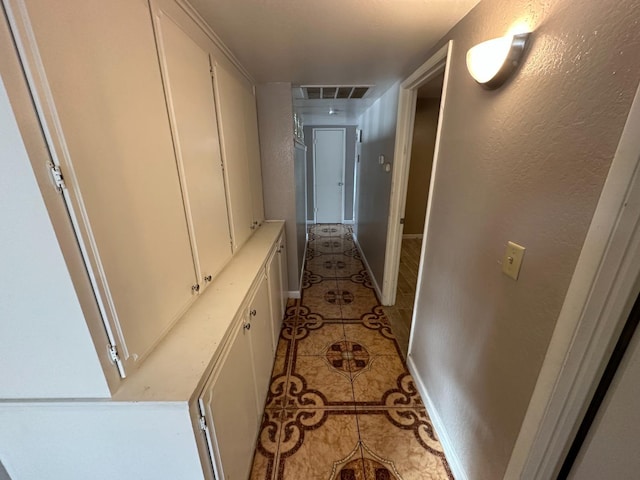 corridor with a textured wall, light tile patterned flooring, visible vents, and baseboards