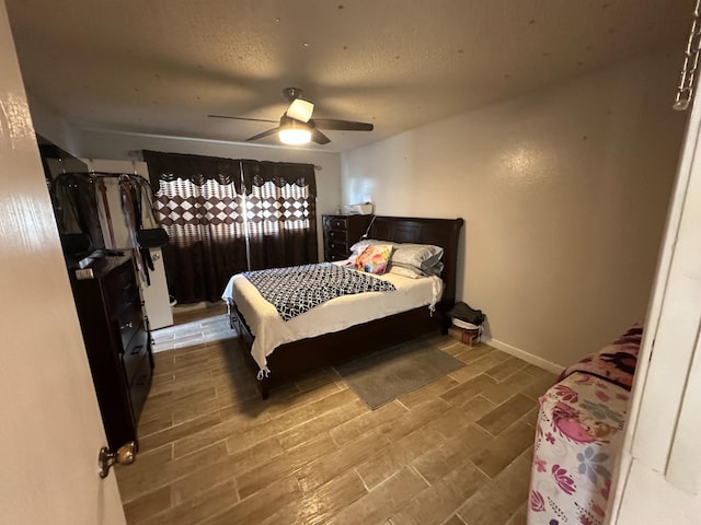 bedroom with a textured ceiling, baseboards, a ceiling fan, and wood finish floors