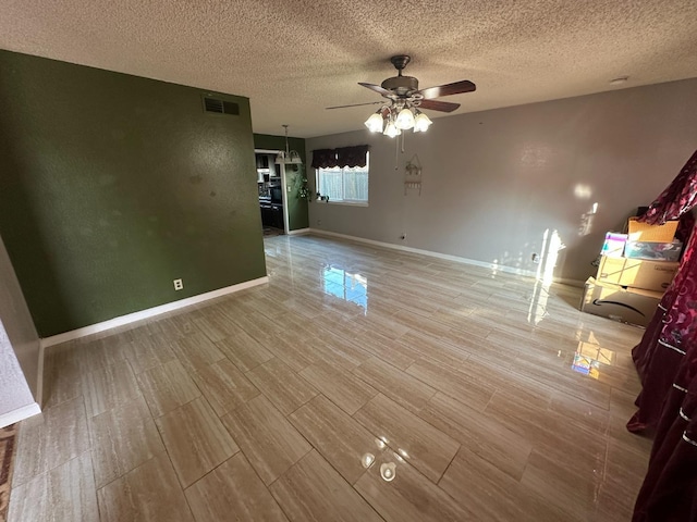 unfurnished living room featuring visible vents, a ceiling fan, a textured ceiling, wood finished floors, and baseboards