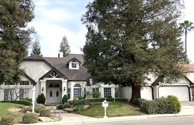 tudor-style house with an attached garage, driveway, a front lawn, and stucco siding