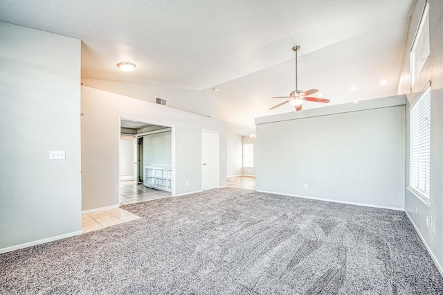 empty room featuring visible vents, a ceiling fan, light colored carpet, lofted ceiling, and light tile patterned flooring