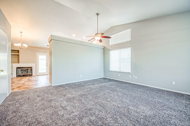 carpeted empty room featuring a fireplace, vaulted ceiling, a wealth of natural light, and ceiling fan with notable chandelier