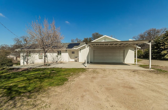 ranch-style home with stucco siding, an attached garage, a front yard, roof mounted solar panels, and driveway