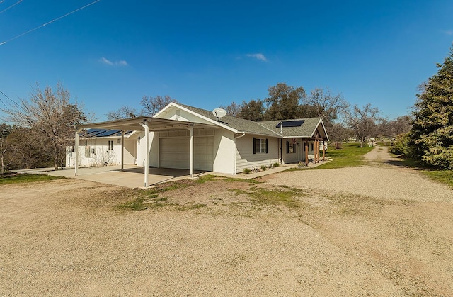 exterior space with an attached garage, solar panels, dirt driveway, and a carport