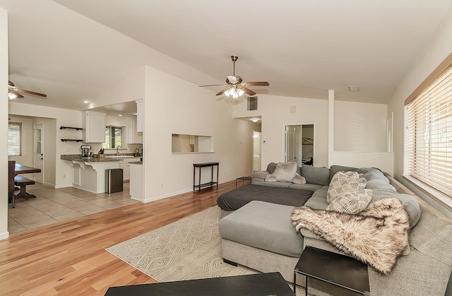 living area with light wood-style floors, a wealth of natural light, ceiling fan, and lofted ceiling