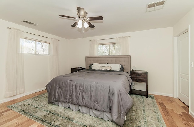 bedroom with ceiling fan, wood finished floors, visible vents, and baseboards