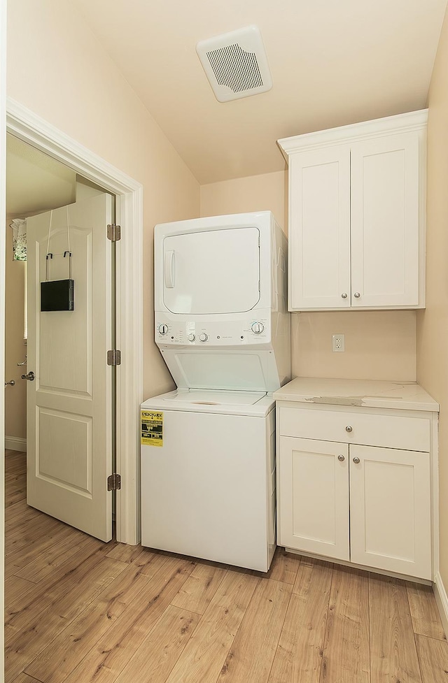 clothes washing area featuring stacked washing maching and dryer, light wood-style flooring, visible vents, and cabinet space