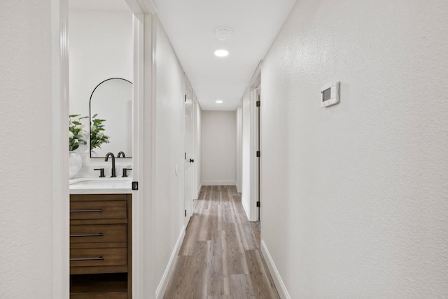 corridor with light wood-style floors, a sink, and baseboards