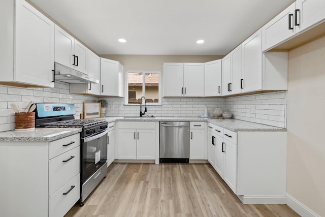 kitchen featuring stainless steel appliances, light wood-style floors, a sink, light stone countertops, and under cabinet range hood