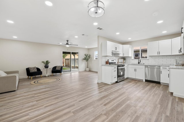 kitchen featuring stainless steel appliances, open floor plan, under cabinet range hood, and decorative backsplash