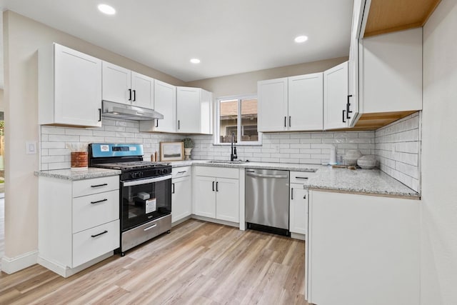 kitchen with under cabinet range hood, stainless steel appliances, a sink, white cabinets, and light wood-type flooring