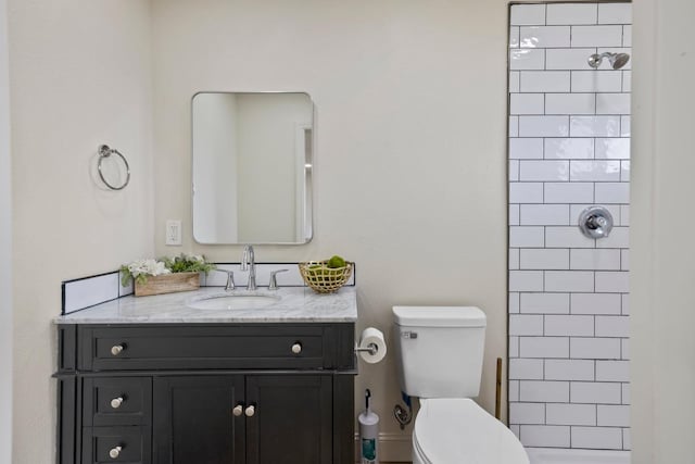 full bathroom featuring tiled shower, vanity, and toilet