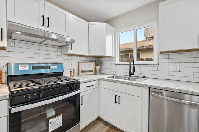 kitchen with stainless steel appliances, decorative backsplash, white cabinets, a sink, and under cabinet range hood