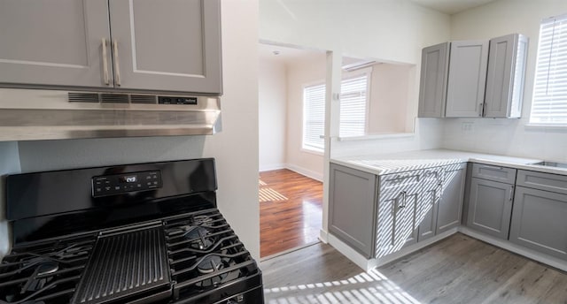 kitchen featuring black gas range, under cabinet range hood, gray cabinets, backsplash, and light wood finished floors