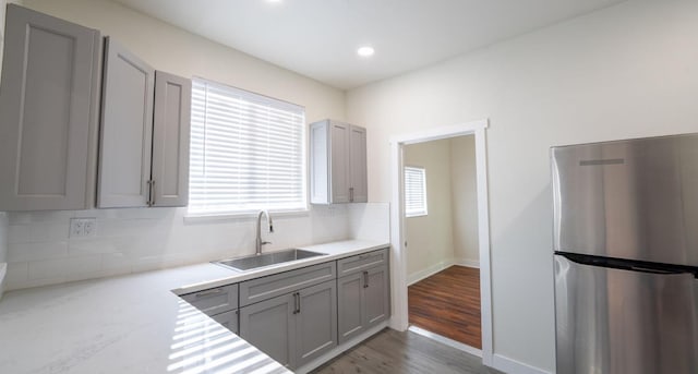 kitchen with decorative backsplash, wood finished floors, freestanding refrigerator, gray cabinets, and a sink