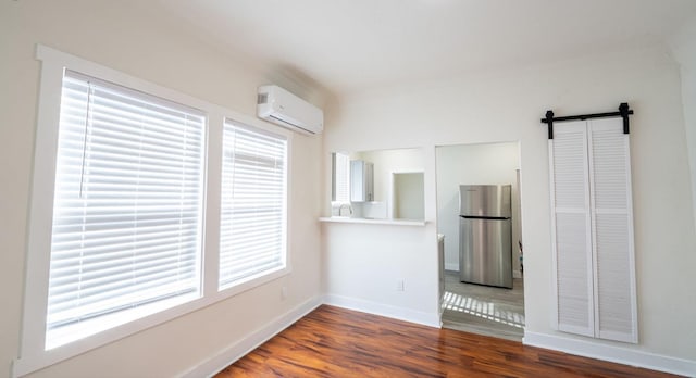 unfurnished room with wood finished floors, an AC wall unit, baseboards, and a barn door