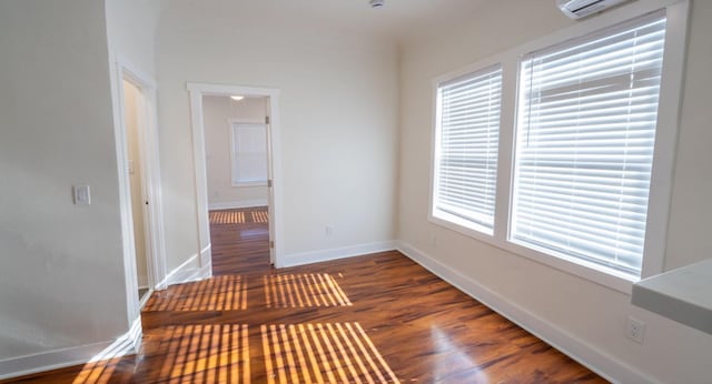 empty room with a wall unit AC, baseboards, and wood finished floors